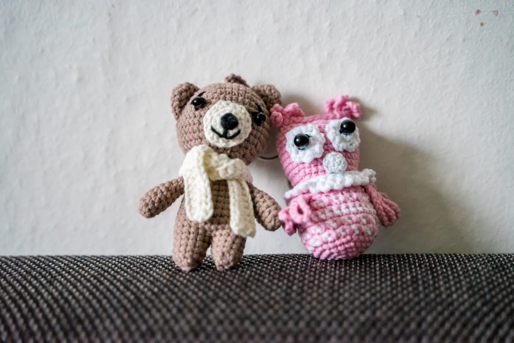 A crocheted brown bear and pink owl amigurumi toy side by side