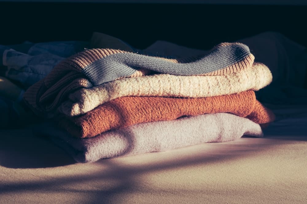 A stack of folded knit sweaters in cream, rust, and grey tones